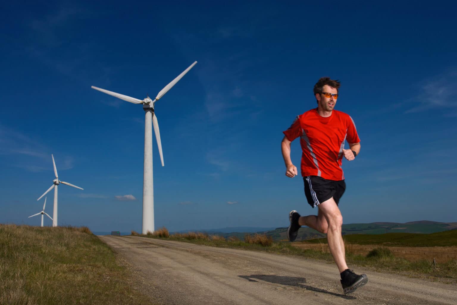 Man running with windmills behind and blue sky - how to run faster - 15 ways